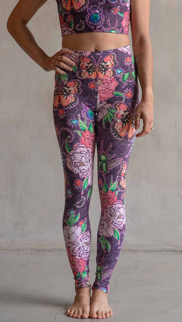 Front view of model wearing WERKSHOP Enchanted Garden Athleisure Leggings. The fabric is printed with original artwork by our Female Founder, Chriztina Marie. The artwork printed not the fabric features Butterflies, Beetles and Peonies over a warm fuchsia with bright bold pops of color on each beetle and Butterfly.