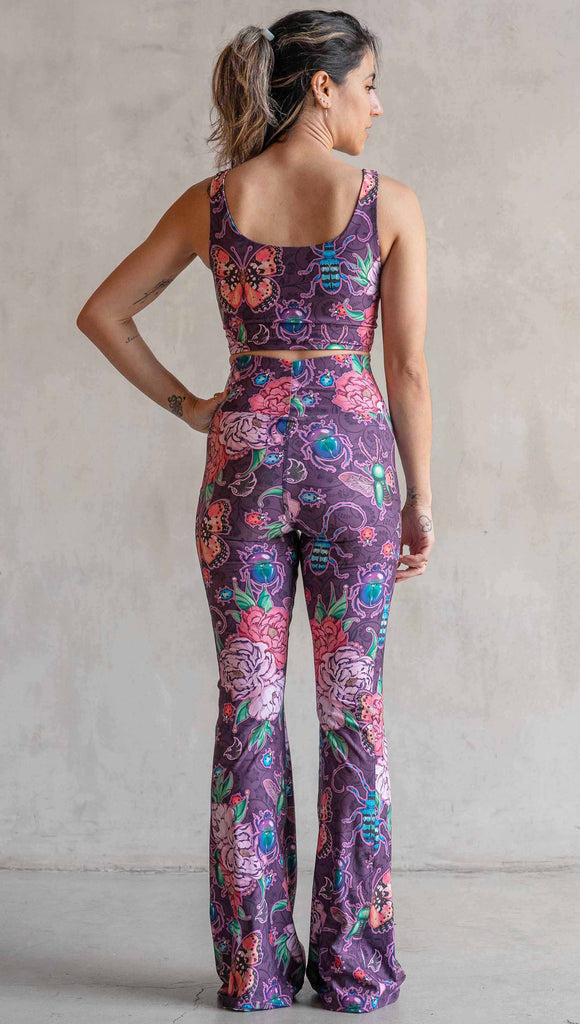 Full body back view of model wearing WERKSHOP Enchanted Garden EnviSoft Bell Bottom pants with Pockets. The fabric is printed with original artwork by our Female Founder, Chriztina Marie. The artwork printed not the fabric features Butterflies, Beetles and Peonies over a warm fuchsia with bright bold pops of color on each beetle and Butterfly.
