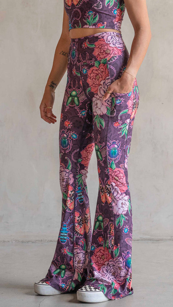 Side view of model wearing WERKSHOP Enchanted Garden EnviSoft Bell Bottom pants with Pockets. The fabric is printed with original artwork by our Female Founder, Chriztina Marie. The artwork printed not the fabric features Butterflies, Beetles and Peonies over a warm fuchsia with bright bold pops of color on each beetle and Butterfly.