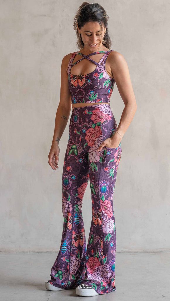 Full body front view of model wearing WERKSHOP Enchanted Garden EnviSoft Bell Bottom pants with Pockets. The fabric is printed with original artwork by our Female Founder, Chriztina Marie. The artwork printed not the fabric features Butterflies, Beetles and Peonies over a warm fuchsia with bright bold pops of color on each beetle and Butterfly.
