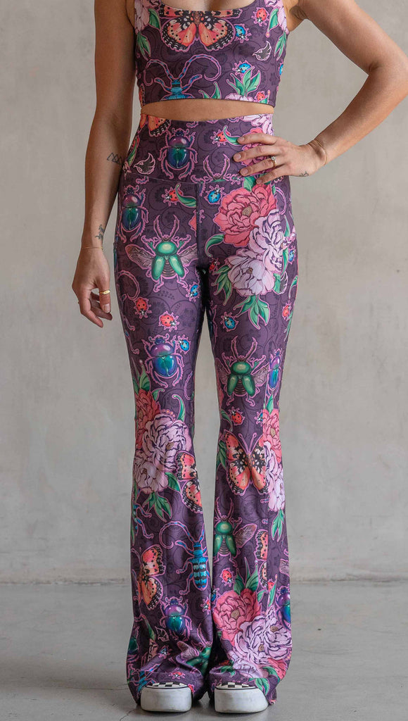 Front view of model wearing WERKSHOP Enchanted Garden EnviSoft Bell Bottom pants with Pockets. The fabric is printed with original artwork by our Female Founder, Chriztina Marie. The artwork printed not the fabric features Butterflies, Beetles and Peonies over a warm fuchsia with bright bold pops of color on each beetle and Butterfly.
