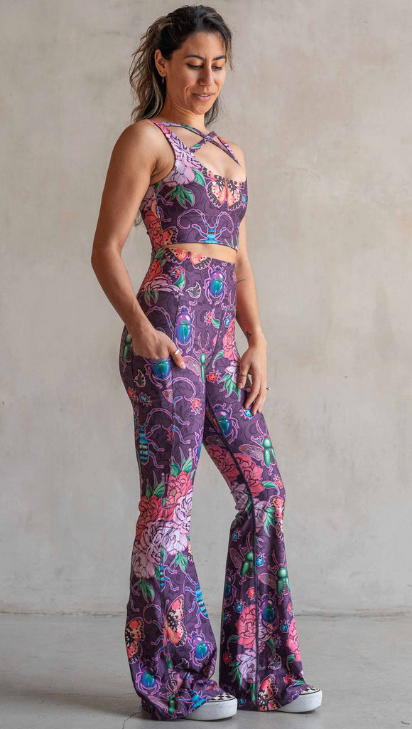 Full body front view of model wearing WERKSHOP Enchanted Garden EnviSoft Bell Bottom pants with Pockets. The fabric is printed with original artwork by our Female Founder, Chriztina Marie. The artwork printed not the fabric features Butterflies, Beetles and Peonies over a warm fuchsia with bright bold pops of color on each beetle and Butterfly.