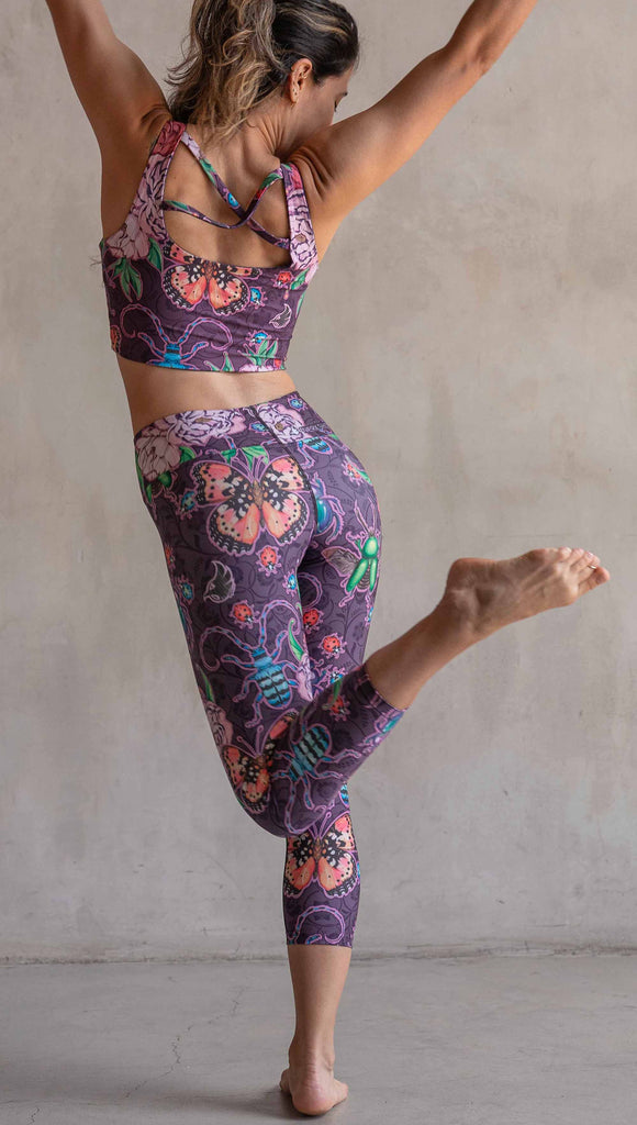 Back view of model wearing WERKSHOP Enchanted Garden Capri Length Triathlon Leggings. The fabric is printed with original artwork by our Female Founder, Chriztina Marie. The artwork printed not the fabric features Butterflies, Beetles and Peonies over a warm fuchsia with bright bold pops of color on each beetle and Butterfly.