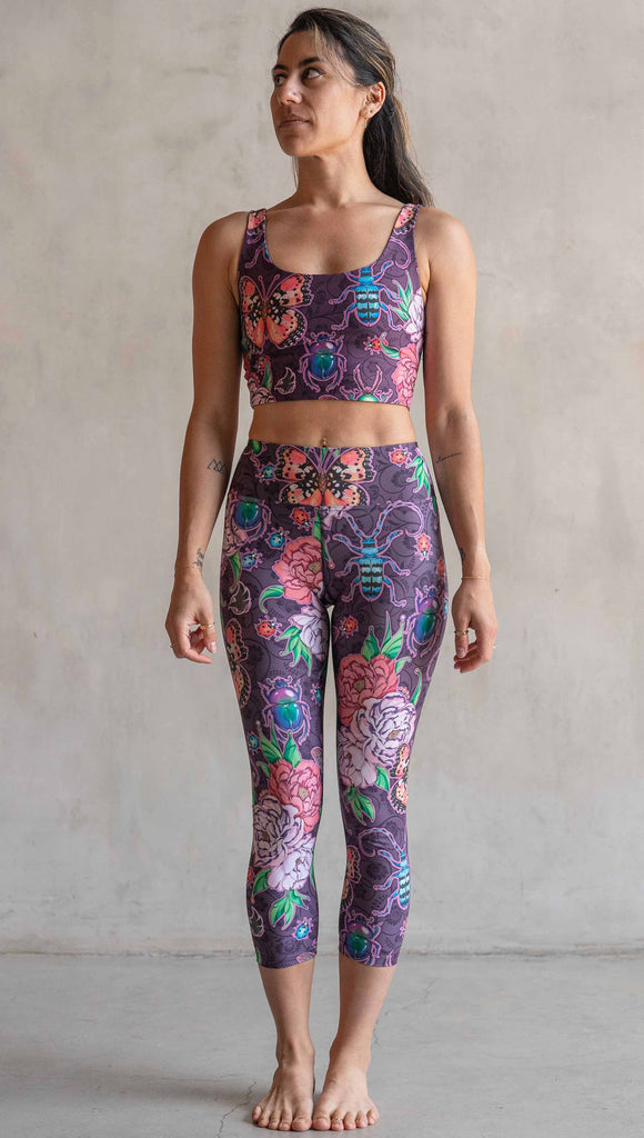 Front view of model wearing WERKSHOP Enchanted Garden Capri Length Triathlon Leggings. The fabric is printed with original artwork by our Female Founder, Chriztina Marie. The artwork printed not the fabric features Butterflies, Beetles and Peonies over a warm fuchsia with bright bold pops of color on each beetle and Butterfly.
