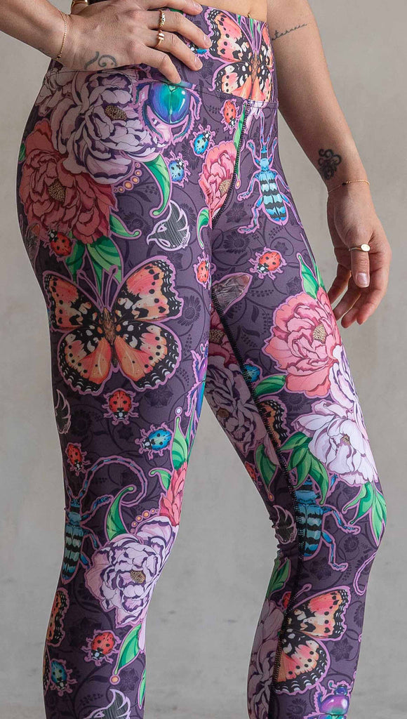 Zoomed in view of model wearing WERKSHOP Enchanted Garden Capri Length Triathlon Leggings. The fabric is printed with original artwork by our Female Founder, Chriztina Marie. The artwork printed not the fabric features Butterflies, Beetles and Peonies over a warm fuchsia with bright bold pops of color on each beetle and Butterfly.