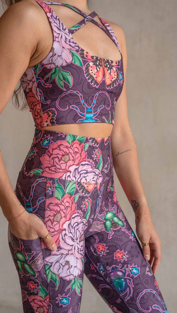 Zoomed in view of model wearing WERKSHOP Enchanted Garden EnviSoft Leggings with Pockets. The fabric is printed with original artwork by our Female Founder, Chriztina Marie. The artwork printed not the fabric features Butterflies, Beetles and Peonies over a warm fuchsia with bright bold pops of color on each beetle and Butterfly.