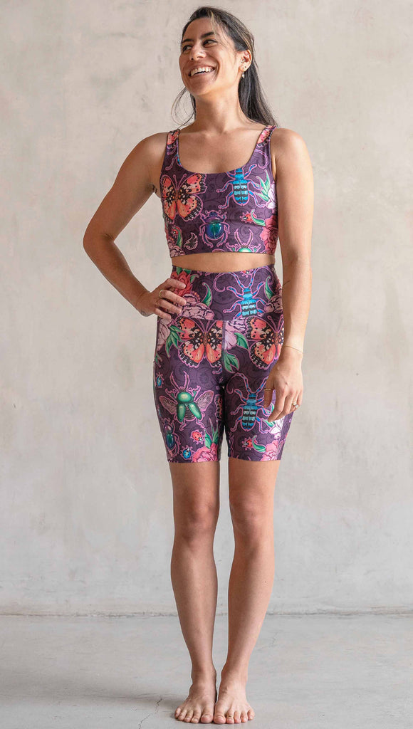 Full body front view of model wearing WERKSHOP Enchanted Garden EnviSoft Bicycle length shorts with pockets. The fabric is printed with original artwork by our Female Founder, Chriztina Marie. The artwork printed not the fabric features Butterflies, Beetles and Peonies over a warm fuchsia with bright bold pops of color on each beetle and Butterfly.