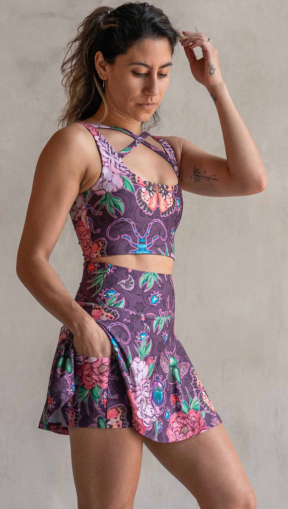 Side view of model wearing WERKSHOP Enchanted Garden EnviSoft Active Skirt with hidden shorts and Pockets. The fabric is printed with original artwork by our Female Founder, Chriztina Marie. The artwork printed not the fabric features Butterflies, Beetles and Peonies over a warm fuchsia with bright bold pops of color on each beetle and Butterfly.