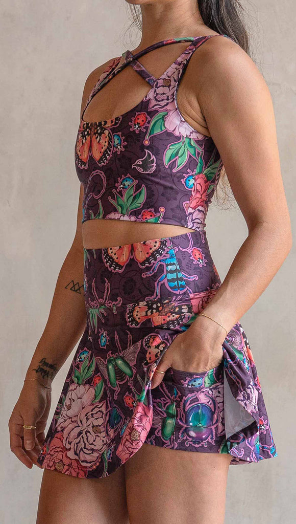 Side view of model wearing WERKSHOP Enchanted Garden EnviSoft Active Skirt with hidden shorts and Pockets. The fabric is printed with original artwork by our Female Founder, Chriztina Marie. The artwork printed not the fabric features Butterflies, Beetles and Peonies over a warm fuchsia with bright bold pops of color on each beetle and Butterfly.