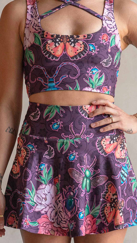 Zoomed in view of model wearing WERKSHOP Enchanted Garden EnviSoft Active Skirt with hidden shorts and Pockets. The fabric is printed with original artwork by our Female Founder, Chriztina Marie. The artwork printed not the fabric features Butterflies, Beetles and Peonies over a warm fuchsia with bright bold pops of color on each beetle and Butterfly.