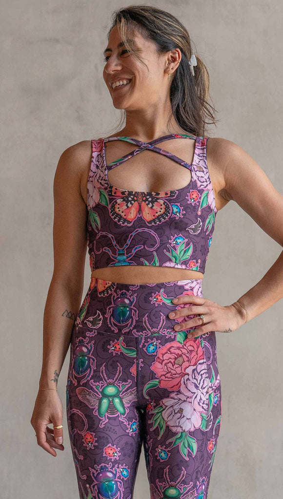 Front view of model wearing WERKSHOP Starlings and Enchanted Garden 4-Way reversible top. The fabric is printed with original artwork by Chriztina Marie. One side features European Starlings perched on a branch near a crescent moon and fireflies. The colors are warm purples with pops of pink, gold and green. The other side features Butterflies, Beetles and Peonies over a warm fuchsia with bright bold pops of color on each beetle and Butterly.