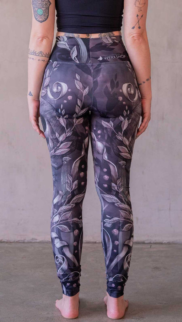 Model wearing WERKSHOP Gothica leggings featuring original and exclusive artwork of a human skull with ornate details and foliage over a smokey gray background with hints of dark mauve and purple tones.
