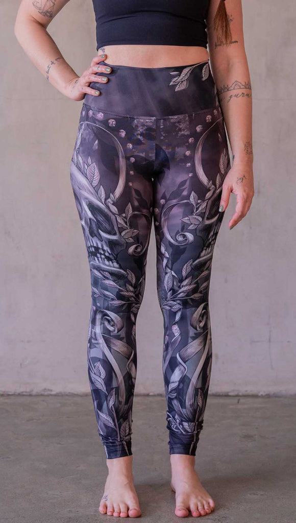 Model wearing WERKSHOP Gothica leggings featuring original and exclusive artwork of a human skull with ornate details and foliage over a smokey gray background with hints of dark mauve and purple tones.