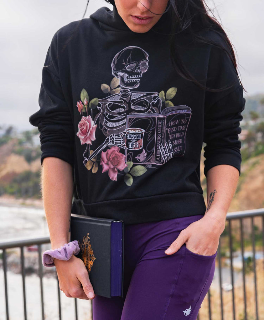 Girl holding a book while wearing WERKSHOP "Death by TBR" Hoodie and Amethyst EnviSoft Leggings