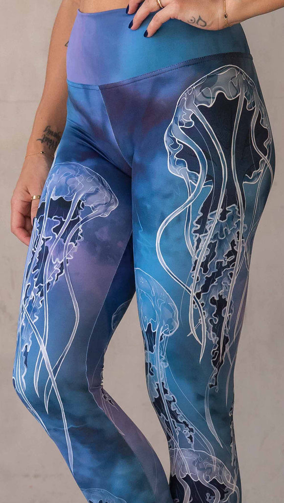 Zoomed in view of model wearing WERKSHOP Jellyfish Athleisure Leggings. The artwork on the leggings shows white jellyfish swimming up the wearer's legs over a cobalt blue and purple watercolor background.