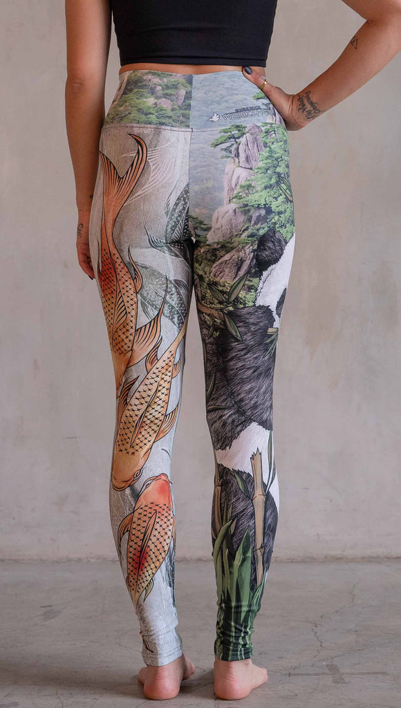 Model wearing WERKSHOP Koi Fish and Giant Panda Mashup Leggings. The wearer's right leg has an illustration of a panda eating bamboo with a gorgeous background of mountains. The wearers right leg has koi fishies swimming over an abstract taupe and forest green background.