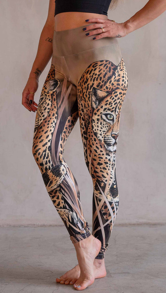Model wearing WERKSHOP Leopard Leggings. The leggings feature original and exclusive artwork of a Leopard walking through the brush. The leggings are all khaki and tan tones with little pops of green in the leopards eyes.