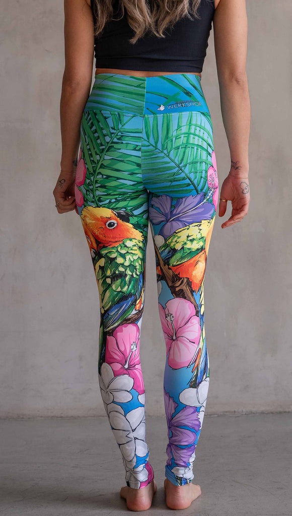 Model wearing WERKSHOP Lovebirds Athleisure Leggings. The leggings feature original and exclusive artwork by Chriztina Marie of two lovebirds snuggling and surrounded by hibiscus flowers. The overall design is very tropical and asymmetrical.