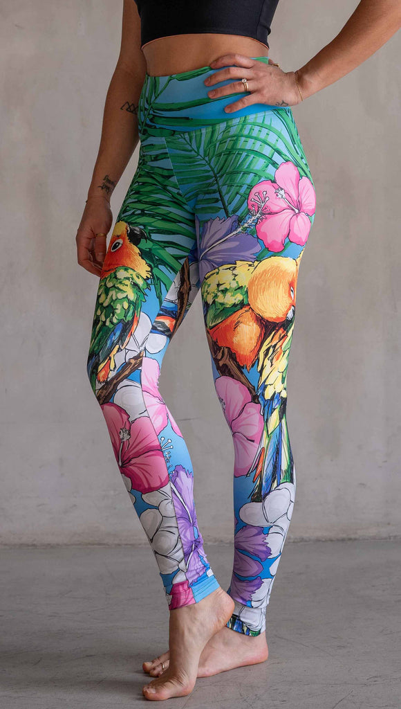 Model wearing WERKSHOP Lovebirds Athleisure Leggings. The leggings feature original and exclusive artwork by Chriztina Marie of two lovebirds snuggling and surrounded by hibiscus flowers. The overall design is very tropical and asymmetrical.