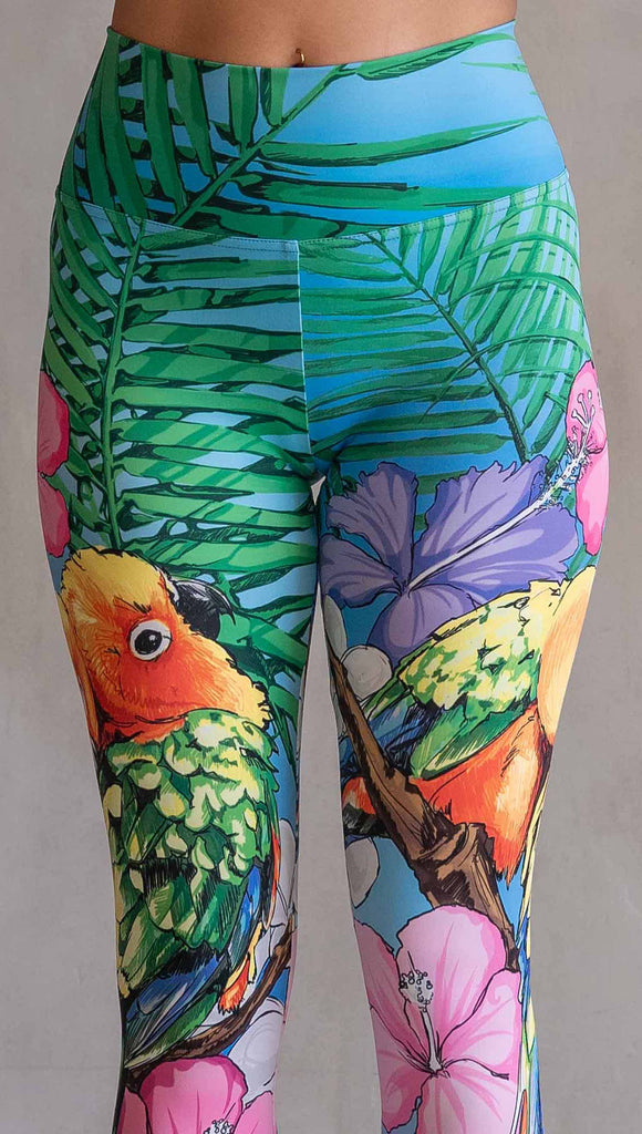 Zoomed in photo of model wearing WERKSHOP Lovebirds Athleisure Leggings. The leggings feature original and exclusive artwork by Chriztina Marie of two lovebirds snuggling and surrounded by hibiscus flowers. The overall design is very tropical and asymmetrical.