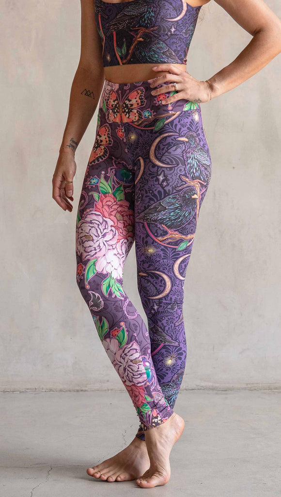 Side view of model wearing WERKSHOP Starlings and Enchanted Garden Mashup Leggings. The fabric is printed with original artwork by Chriztina Marie. Each leg features different artwork. The wearer’s left leg has European Starlings perched on a branch near a crescent moon and fireflies. The colors are warm purples with pops of pink, gold and green. The wearer’s right leg features Butterflies, Beetles and Peonies over a warm fuchsia with bright bold pops of color on each beetle and Butterly.