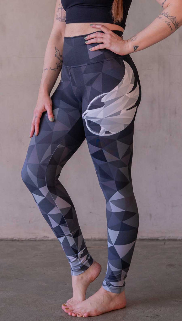 Model wearing WERKSHOP Onyx leggings featuring original and exclusive polygon artwork that has a dark gray and black at the waistband to light gray ombre fade below the knee. The design is asymmetrical with the WERKSHOP eagle logo is on the wearers left hip. 