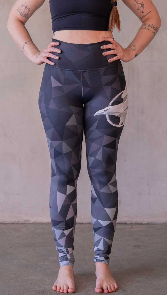 Model wearing WERKSHOP Onyx leggings featuring original and exclusive polygon artwork that has a dark gray and black at the waistband to light gray ombre fade below the knee. The design is asymmetrical with the WERKSHOP eagle logo is on the wearers left hip. 