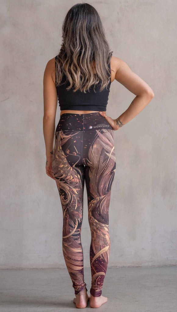 Model wearing WERKSHOP Phoenix Athleisure Leggings. The leggings are printed with a mythical phoenix swirling up each leg with embers flying through the background. The overall color theme is super earthy and warm browns, oranges and yellow tones