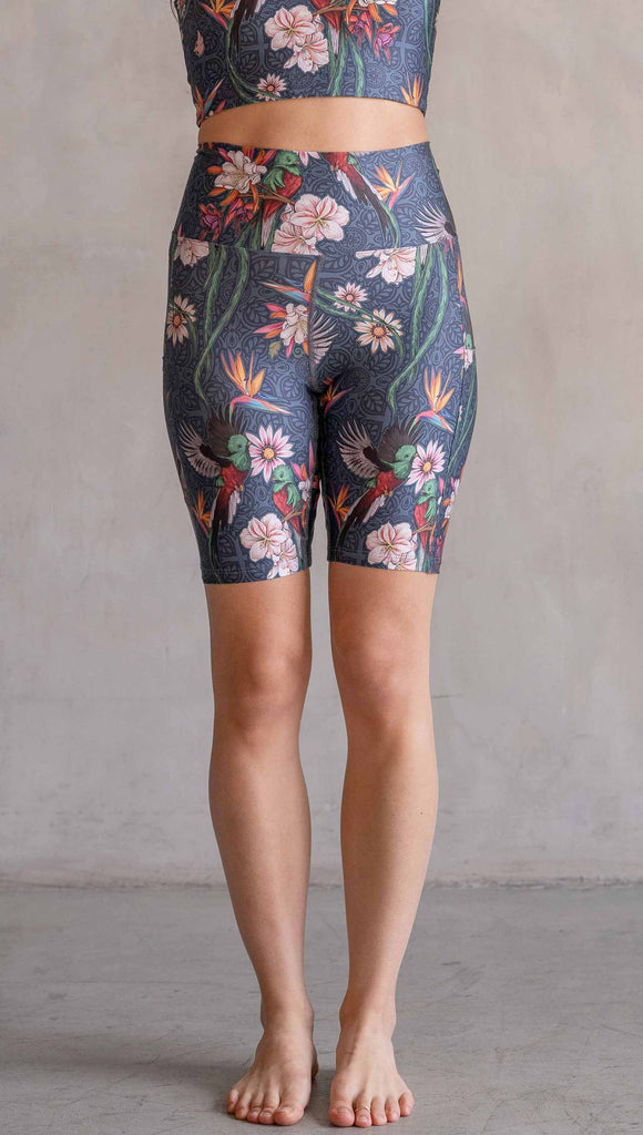 Model wearing WERKSHOP Quetzal Featherlight Bicycle length shorts. The shorts are printed with with original quetzal artwork with clusters of tropical flowers and birds of paradise over a blue background. The featherlight shirt have pockets.