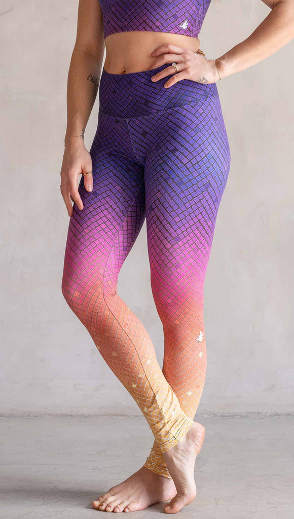 Model wearing WERKSHOP Rainbow Mosaic Athlesiure Leggings and matching top. The leggings are printed with what look like tiny mosaic tiles in an ombre effect from purple at the waistband, to pink at the knee ... then coral and a soft warm yellow at the leg opening.