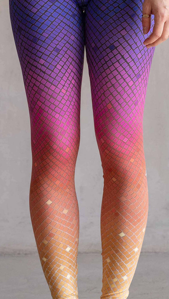 Zoomed in view of model wearing WERKSHOP Rainbow Mosaic Athlesiure Leggings and matching top. The leggings are printed with what look like tiny mosaic tiles in an ombre effect from purple at the waistband, to pink at the knee ... then coral and a soft warm yellow at the leg opening.