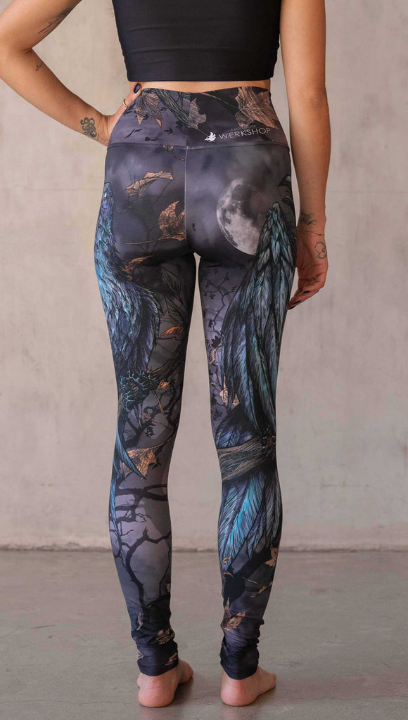 Girl wearing WERKSHOP "Raven" athleisure leggings. The artwork on the leggings feature a raven perched on a branch looking into the moonlight with pops of blue glistening from his feathers. He is framed by autumn leaves over a very spooky night sky.