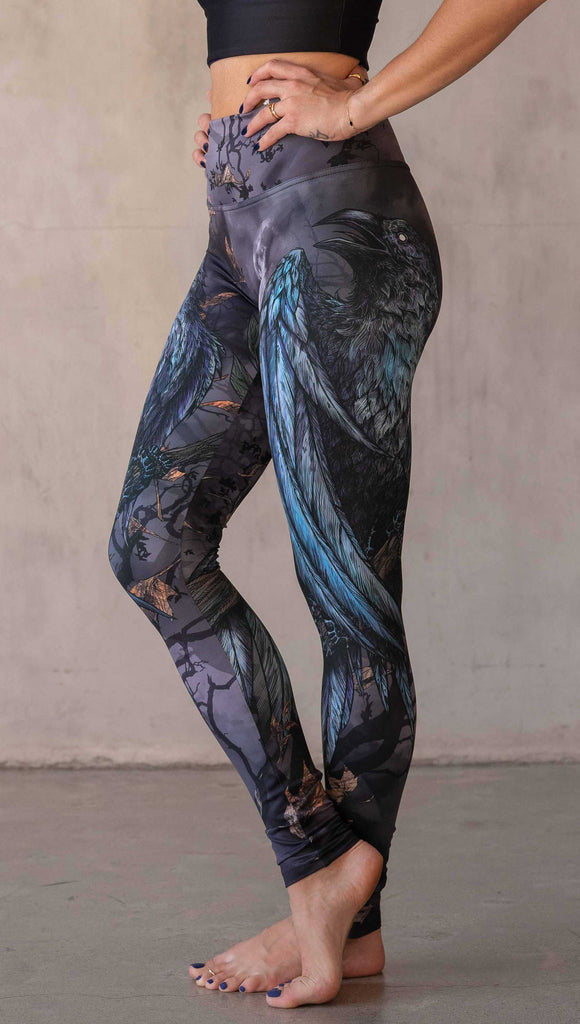 Girl wearing WERKSHOP "Raven" athleisure leggings. The artwork on the leggings feature a raven perched on a branch looking into the moonlight with pops of blue glistening from his feathers. He is framed by autumn leaves over a very spooky night sky.