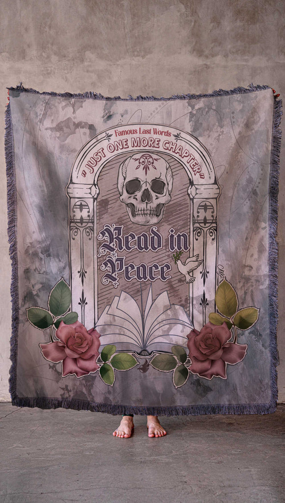 Chenille WERKSHOP Tapestry with original bookish artwork. There is a tombstone with the phrase, "Read in Peace" and "Famous last words: just one more chapter" .. The bottom of the tombstone has an open book with roses framing the base.