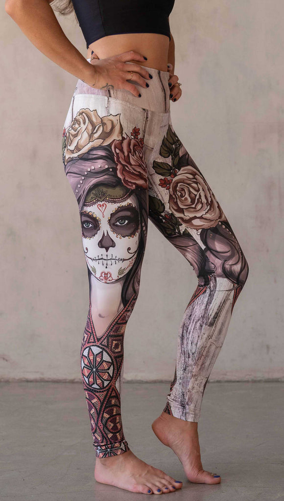 Girl wearing WERKSHOP "Remix" SugarSkull Athelisure leggings. The artwork printed on the leggings features a girl wearing Dia De Los Muertos makeup with a crown of roses and a beaded necklace with a romantic color woodgrain background.