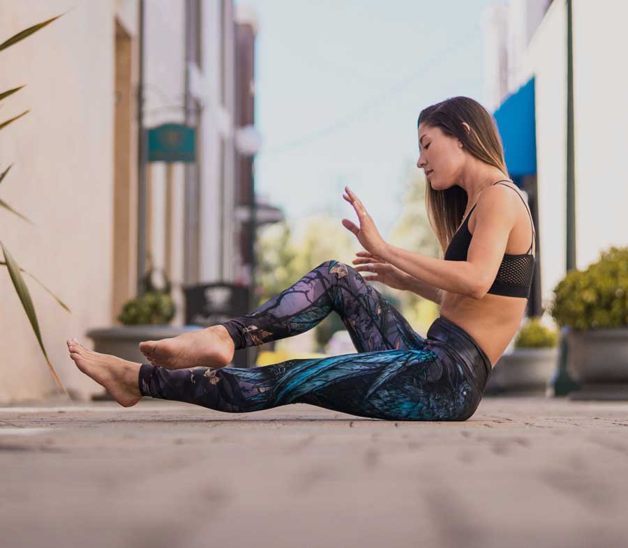 girl photographed in motion, sitting outside on the sidewalk, wearing WERKSHOP Raven Leggings in Triathlon Fabric