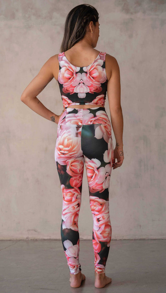 Girl wearing WERKSHOP Rosaline Floral Athleisure Leggings. The leggings feature a fun geometric floral print. It has bright pink flowers with pops of bright peach/orange hues. The flowers are over a super dark blackish greenish background