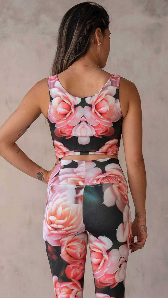 Girl wearing the WERKSHOP Reversible Artichoke and Rosaline Top. This image shows the Rosaline side. It has bright pink flowers with pops of bright peach/orange hues. The flowers are over a super dark blackish greenish background