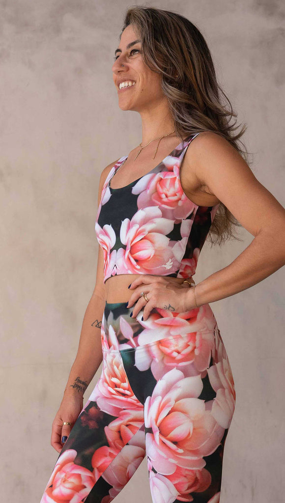 Girl wearing the WERKSHOP Reversible Artichoke and Rosaline Top. This image shows the Rosaline side. It has bright pink flowers with pops of bright peach/orange hues. The flowers are over a super dark blackish greenish background