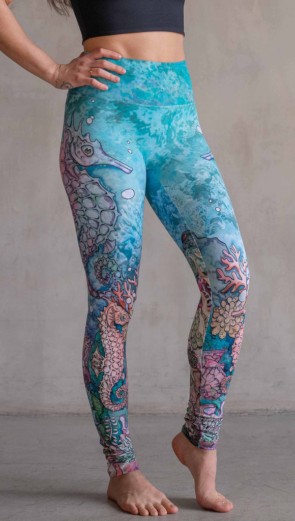 Model wearing WERKSHOP Seahorses Athleisure Leggings. The artwork on the leggings features pastel coloured seahorses and coral reef over an aqua/teal textured background.