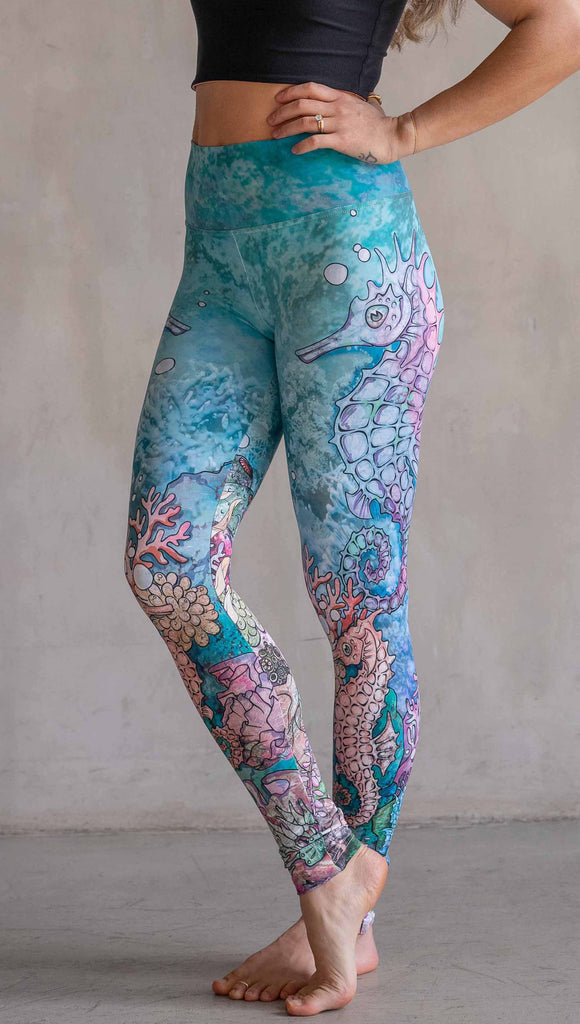 Model wearing WERKSHOP Seahorses Athleisure Leggings. The artwork on the leggings features pastel coloured seahorses and coral reef over an aqua/teal textured background.