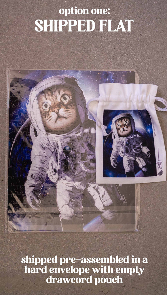 WERKSHOP Space Cat (Catstronaut) Puzzle. The artwork features a house cat wearing an astronaut uniform, floating in outer space with a nebula behind him. Option 1: shiped pre-assembled in a hard envelope with empty drawcord pouch.