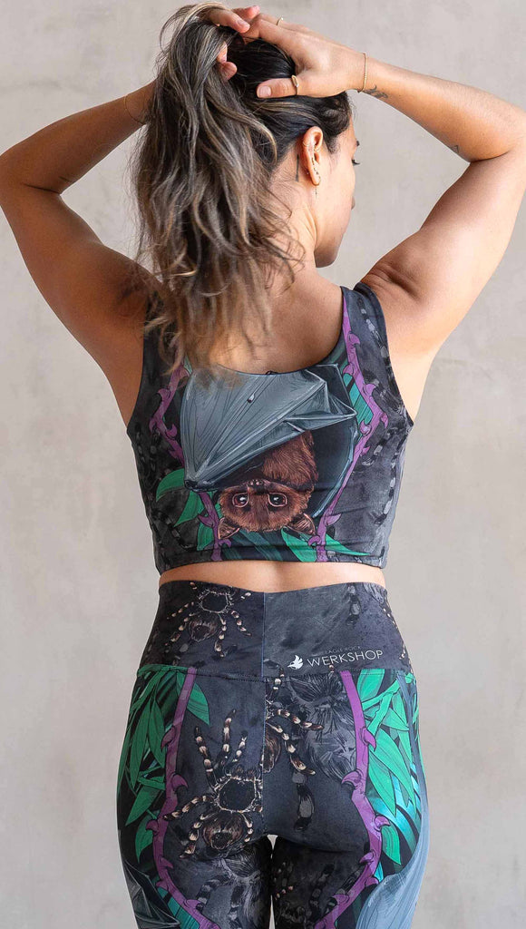 Model wearing WERKSHOP Spooky Season Set. The reversible top features an adorable fruit bat dangling upside down inside a tropical scene with a purple wreath of thorns. The background is a distressed dark gray brushstroke texture. (This version of the artwork has no rats, but does have scattered tarantulas)