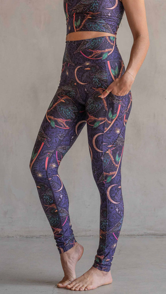 Side view of model wearing WERKSHOP Starlings EnviSoft leggings with pockets. The fabric is printed with original artwork by our Female Founder, Chriztina Marie. Featuring European Starlings perched on a branch near a crescent moon and fireflies. The colors are warm purples with pops of pink, gold and green.