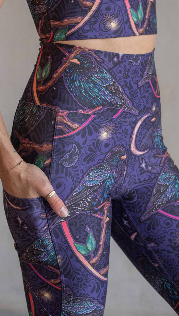 Zoomed in photo of model wearing WERKSHOP Starlings EnviSoft leggings with pockets. The fabric is printed with original artwork by our Female Founder, Chriztina Marie. Featuring European Starlings perched on a branch near a crescent moon and fireflies. The colors are warm purples with pops of pink, gold and green.