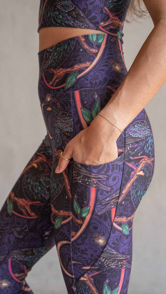 Zoomed in view of model wearing WERKSHOP Starlings EnviSoft leggings with pockets. The fabric is printed with original artwork by our Female Founder, Chriztina Marie. Featuring European Starlings perched on a branch near a crescent moon and fireflies. The colors are warm purples with pops of pink, gold and green.
