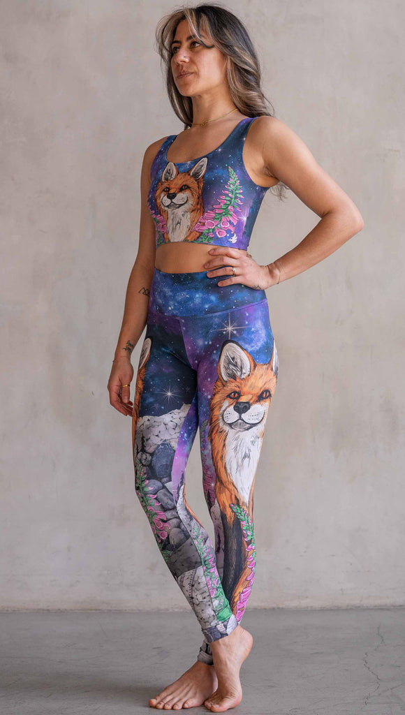 Girl wearing WERKSHOP X Save A Fox Athleisure Leggings. The artwork on the leggings features a coy red fox looking upward while perched on a rock and framed with foxglove flowers. The background for the artwork features a galactic sky with swirls of purple and blue and sparkling stars.