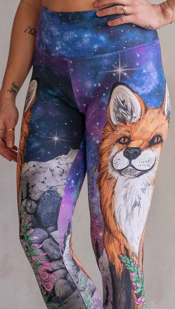 Zoomed in view of girl wearing WERKSHOP X Save A Fox Athleisure Leggings. The artwork on the leggings features a coy red fox looking upward while perched on a rock and framed with foxglove flowers. The background for the artwork features a galactic sky with swirls of purple and blue and sparkling stars.