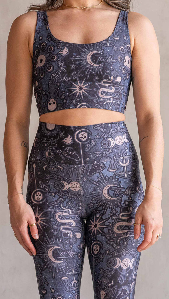 Model wearing WERKSHOP Zodiac Tennis Skirt with built-in shorts. They are high waist and feature pockets on both legs under the flirty skirt. The blue/tarot artwork has skulls, snakes, moons and the names of multiple popular tarot cards like "Strength, Lovers, Death and The Hanged Man"