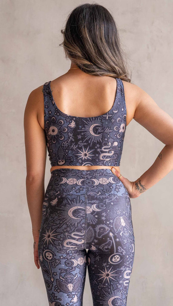 Front view of model wearing WERKSHOP Four-Way Reversible Top. The top has a tarot card themed artwork on a dark blue background on one side and a zodiac themed artwork on purple background on the opposite side. She is wearing it with the Blue side out and the X neckline detail in the back.